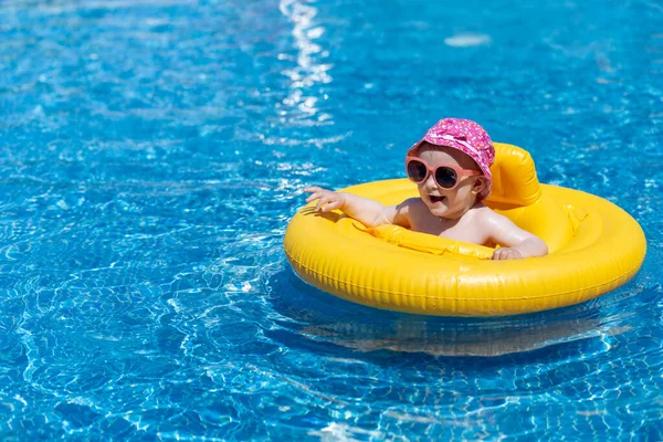Cute little girl in swimming pool with swimming float, wearing sunglasses and colorful hat. Children and summer season concept.