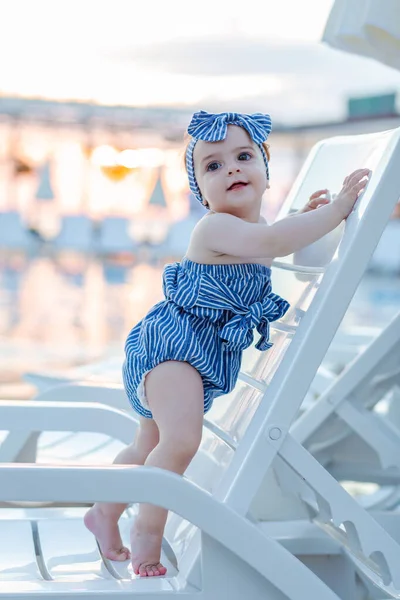 Cute little toddler baby girl standing on sunbed. Summer season resort concept. Space for copy.