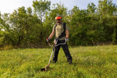 Man mowing the grass at his garden by using string trimmer with protective helmet and gloves.