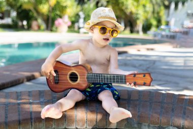 Havuz başında gitar çalan küçük bir çocuğun portresi. Yaz tatili müzik konsepti.