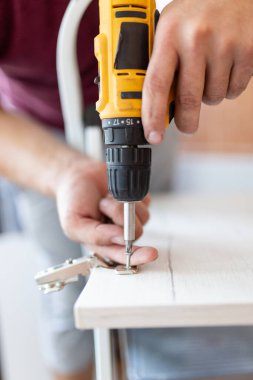 Close up of man assembling furniture by using cordless screwdriver
