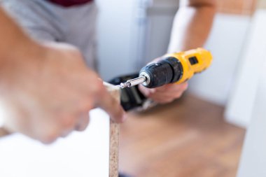 Close up of man holding electrical battery screwdriver while installing wooden kitchen shelves
