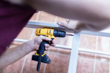 Evde kablosuz tornavida kullanarak mutfak rafı kuran işçiyi kapat.