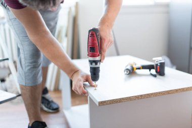 Furniture Installation. Man Using Electric Drill Assembling And Fixing Wooden Shelf Furnishing Room At Home.