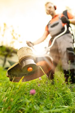 Close up of string grass cutting trimmer held by worker in protective clothing. Gardening concept.