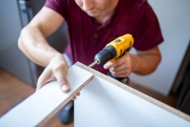 Close up of man holding electrical battery screwdriver while installing wooden kitchen shelves