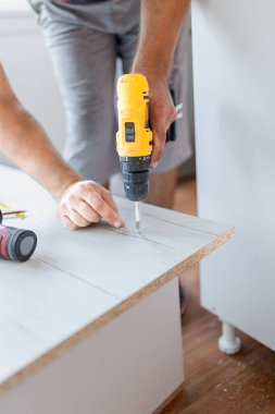 Mobilya kurulumu. Elektirikli tornavida kullanan adam evdeki ahşap mobilya odasını monte edip tamir ediyor..