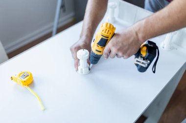 Man installing wooden shelves by using cordless screwdriver
