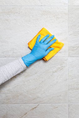Kadın elinin koruyucu eldiveni içinde banyoda seramik fayansları mikrofiber bezle yıkıyor..