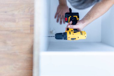 Close up of man holding electrical battery screwdriver while installing wooden kitchen shelves