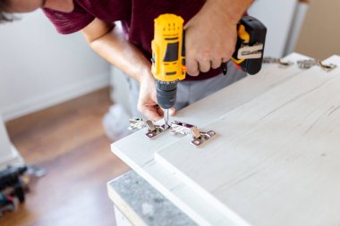 Elinde kablosuz tornavida tutan adam ve evde mobilya montajı yaparken vida vida vidaları yalan söylüyor.