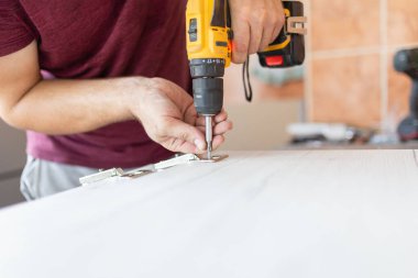 Kablosuz tornavida kullanan ve evde mobilya montajı yapan bir vidayı vidalayan adam yalan söylüyor.