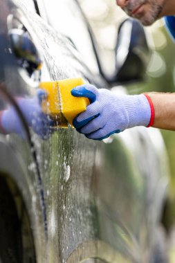 Araba yıkayan işçinin elini koruyucu eldivenle yıka ve arabayı sabunla yıka.
