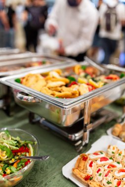 Warming tray with food and people in the background. Party lunch or dinner concept.