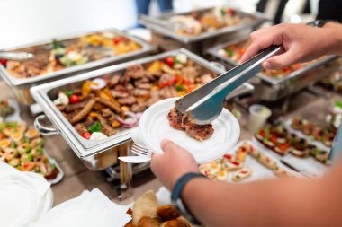 Barbekü ve açık büfe masasında kendine servis yapan bir adam.