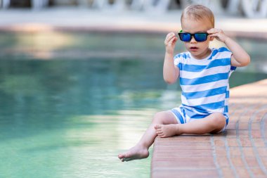 Havuz kenarında oturan şık bir çocuk. Yaz tatili kavramı. Kopyalamak için boşluk.