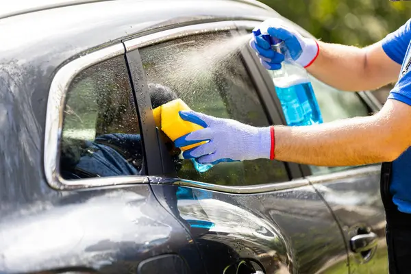 Car wash worker waxing windows by using spray bottle