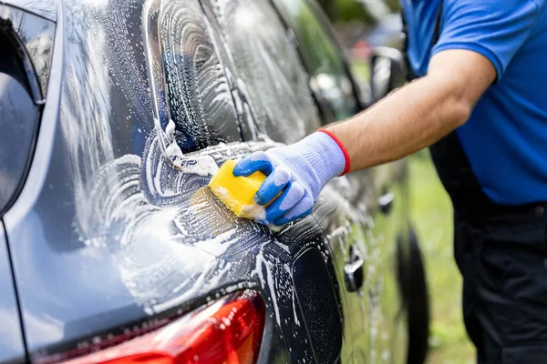 Adam dışarıda sarı süngerle araba yıkıyor.