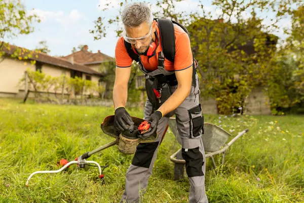 Adam ot biçme mekanizmasını kontrol ediyor. Bahçe araçlarının bakımı.