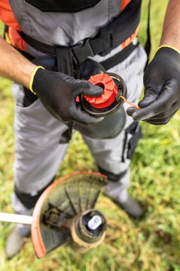 Bahçesinde çim biçmeden önce PF-Man ellerini plastik ipek iplik hattını çekerek kapat. Mevsimlik kavram.