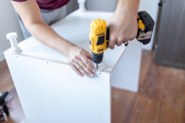 Ahşap mutfak elementlerini monte ederken elinde elektrikli batarya tornavida tutan adama yaklaş.