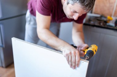 Evde kablosuz tornavida kullanarak mutfak rafı kuran işçiyi kapat.