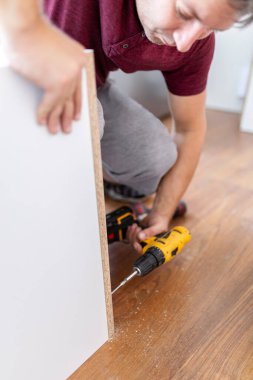 Close up of man holding electrical battery screwdriver while installing wooden kitchen shelves