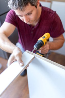 Mutfak ahşap elementlerini monte ederken elinde elektrikli tornavida tutan adam..