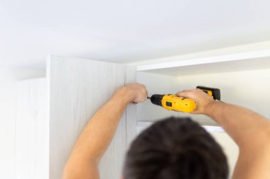 İşçi, kablosuz tornavida kullanarak gizli menteşeyi ahşap kapıya yerleştiriyor.