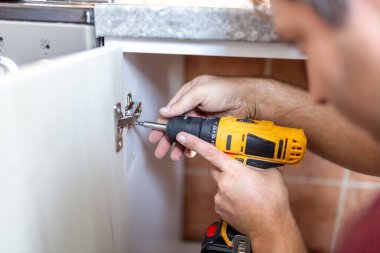 Marangoz mutfak montajını tamamlıyor. Adam mutfağa elektrikli tornavida kullanarak mobilya ve ekipman kuruyor. İnşaat, bakım ve onarım konsepti.