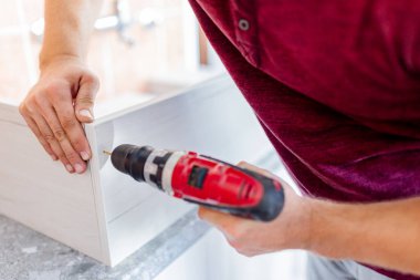Marangoz elektrikli matkap kullanarak çekmecelerden mutfak sandığı kuruyor. Ev yenileme konsepti.