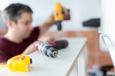 Kablosuz elektrikli matkabı kapat ve arka planda tornavida kullanan bir işçiyle mezurayı ölç. Ev geliştirme kavramı.