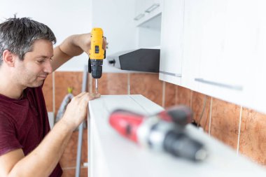 Marangoz elektrikli tornavida kullanarak çekmecelerden mutfak sandığı kuruyor. Ev yenileme konsepti.