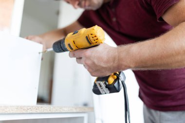 Marangoz elektrikli tornavida kullanarak çekmecelerden mutfak sandığı kuruyor. Ev yenileme konsepti.