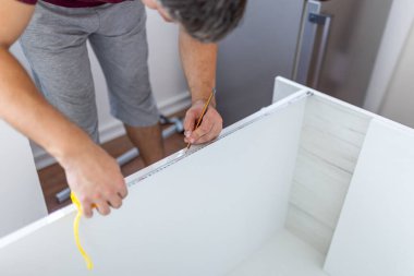 Adam yeni bir mutfak rafı montajı üzerinde çalışıyor ve mezura kullanıyor. Ev geliştirme kavramı.