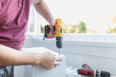 Marangoz elektrikli tornavida kullanarak çekmecelerden mutfak sandığı kuruyor. Ev yenileme konsepti.