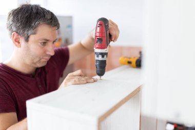 Marangoz elektrikli matkap kullanarak çekmecelerden mutfak sandığı kuruyor. Ev yenileme konsepti.