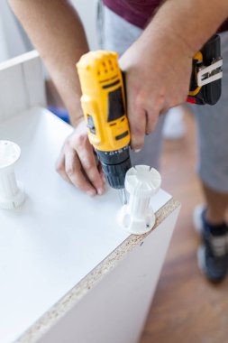 Mobilya toplayıcısı, mutfak ahşap rafı ve bacak montajı için tornavida tutuyor.