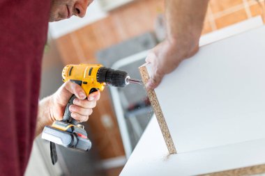 Marangoz elektrikli tornavida kullanarak çekmecelerden mutfak sandığı kuruyor. Ev yenileme konsepti.