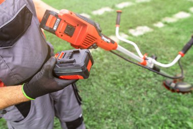 Bahçıvanın elinde kablosuz çim taşıyıcısı ve dışarıda pil varken..