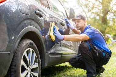 İş yerindeki profesyonel oto yıkama işçisi dışarıda bez parçasıyla araba yıkayıp temizliyor.