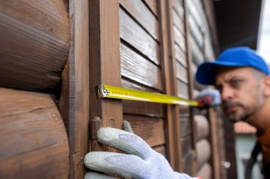 Professional using measure tape for window shutter replacement on wooden house. Home reparation concept.
