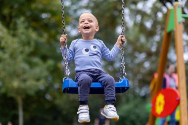 Salıncaktaki neşeli genç çocuğun portresi. Çocuklar dışarıda oyun oynuyor..