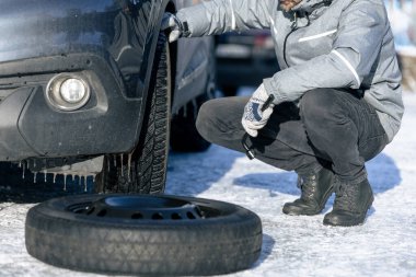 Tekerlek anahtarıyla lastiği patlatan adam. Kışın yol sahnesinde kar yağarken.