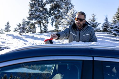 Adam kar fırçası kullanarak arabanın çatısından karı kaldırıyor..