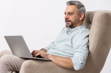 Serbest yazar konsepti. Koltukta oturmuş laptopunu kullanan bir adam. Ev konseptinden uzak çalışma.