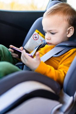 Küçük çocuk arabanın arka koltuğunda otururken akıllı telefon kullanıyor..