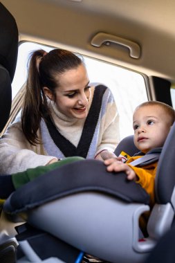 Anne, oğlunun emniyet kemerini arabanın içinde bağlıyor. Aile yolculuğuna hazırlık konsepti.