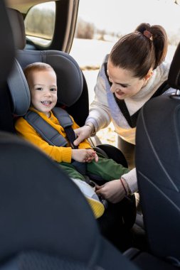 Bebek arabası koltuğu giymiş genç bir çocuk ve kemerini takan bir anne..