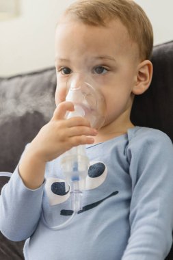 Küçük çocuk evde nebulizörle solunum yapıyor.